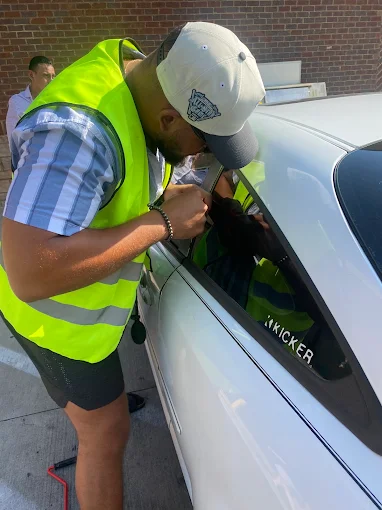 Technician in a safety vest working a wedge tool at a car window to open a locked door