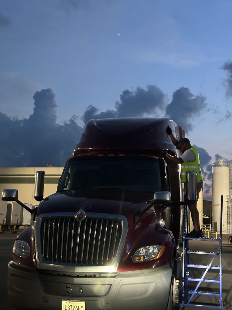 Technician on a rolling work platform beside a semi-truck at dusk